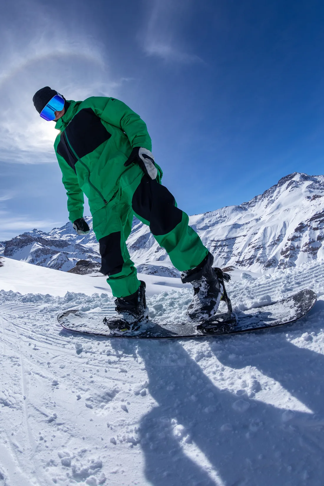 Snowboarder con traje verde sobre su tabla en la montaña.